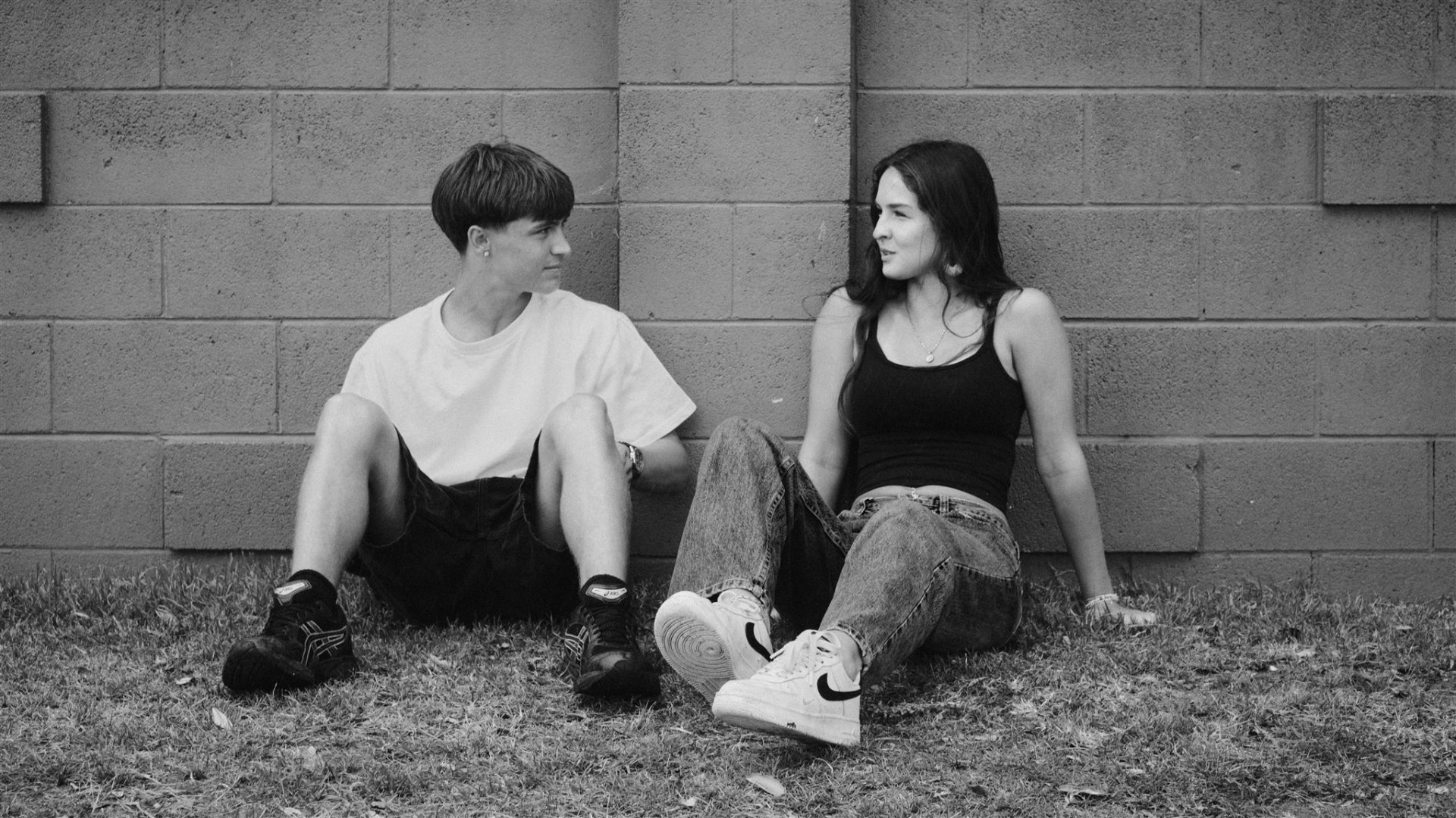 Two young friends leaning against a wall together in Aotearoa